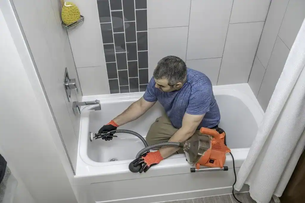 Techniker reinigt die Abflussleitung einer Badewanne mit einer Rohrreinigungsmaschine