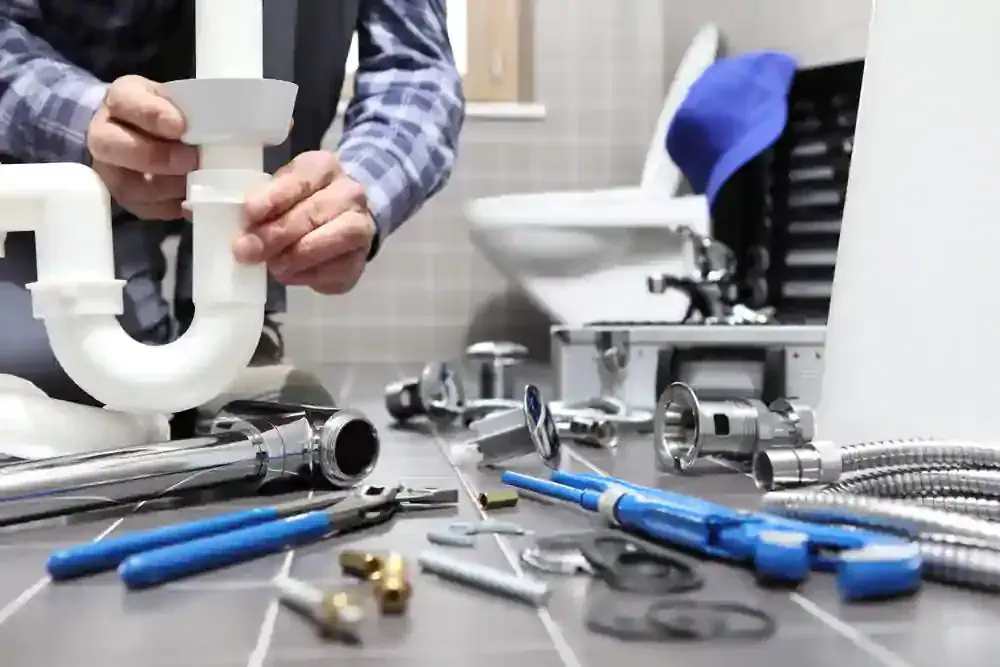 Installateur montiert einen Siphon, daneben Werkzeug und Rohrteile